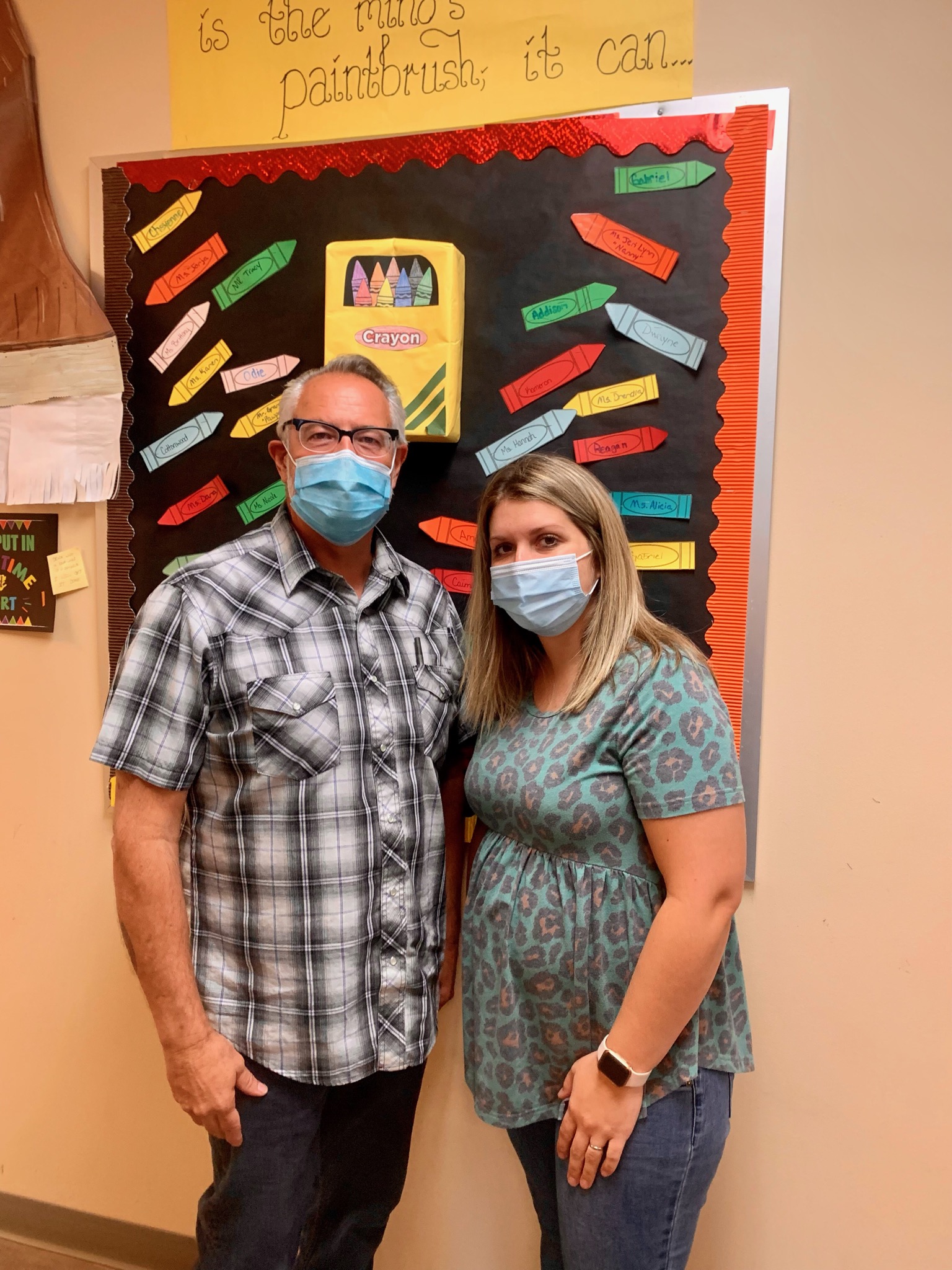 man and woman smiling in front of colorful bulletin board